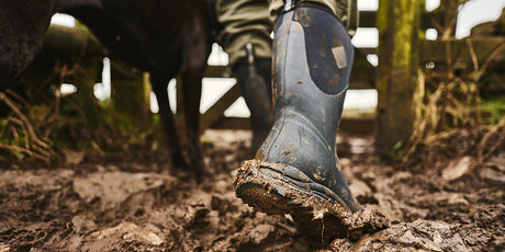 Close-up image of the back of a pair of Muck Boots Arctic Excursion wellingtons being worn on muddy ground