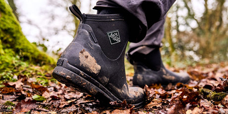 Black Muck Boots ankle boots on a forest floor with a blurred background