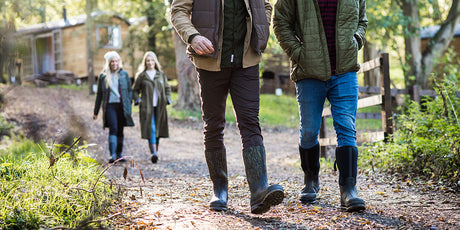 Two men  walking on a path with two women behind in a natural setting with wooden cabins in the background. They are all wearing Muck Boots wellingtons.