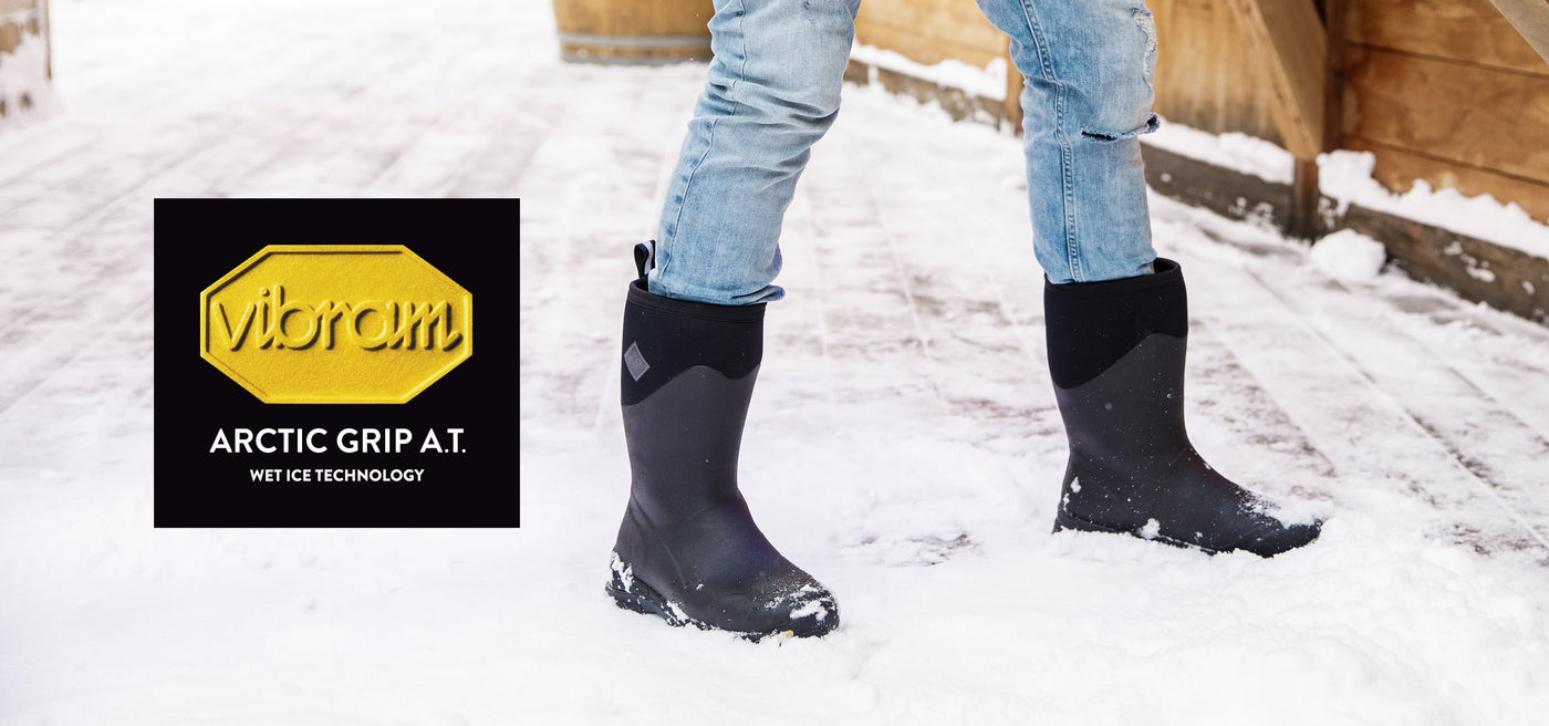 Close-up image of a person stood in snow, wearing a pair of Muck Boots. Vibram logo on left hand side