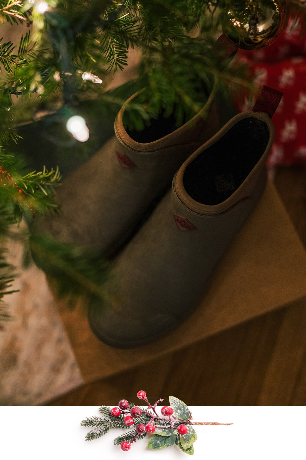 A pair of Muck Boots Muck Originals Pull-On Short Boots below a Christmas tree surrounded by unopened presents. Overlapping image at bottom of snow dusted pine branches, berries and leaves