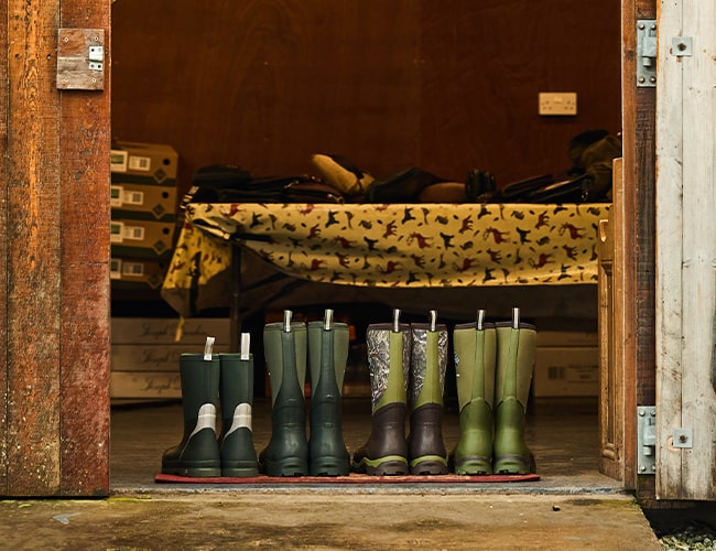 Four pairs of Muck Boots sat on a mat outside of a converted wooden barn