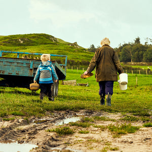 Woman and child walking through a field, the child carrying a bucket and woman two buckets, both wearing Muck Boot wellingtons
