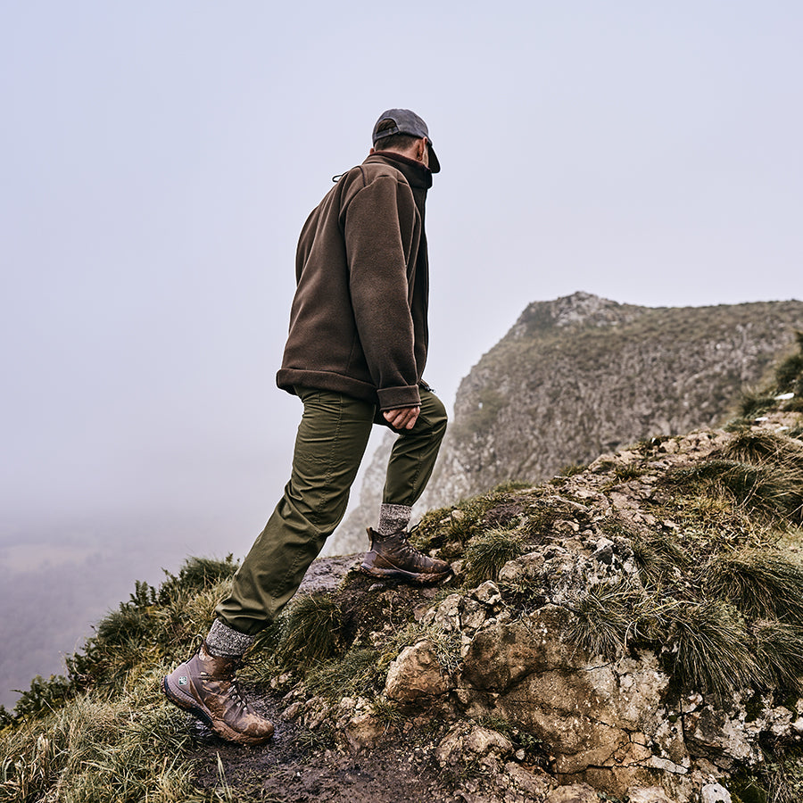 Man walking up a rocky hill, wearing a pair of brown Muck Boot Outscape Max shoes