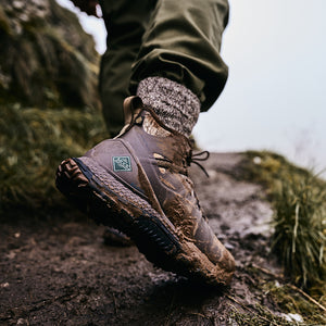 Man walking along a muddy ledge, wearing a pair of lace up Muck Boots
