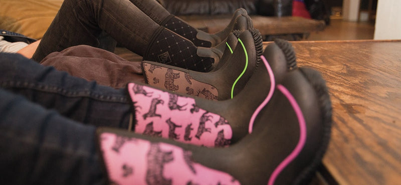 Close up image of children with feet pressed against a table, wearing various styles of Muck Boots wellingtons