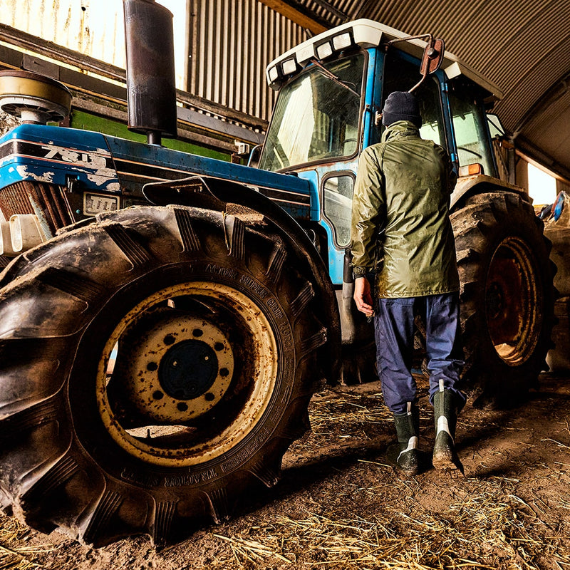 Man approaching a tractor in a barn, wearing a pair of Muck Boots wellingtons