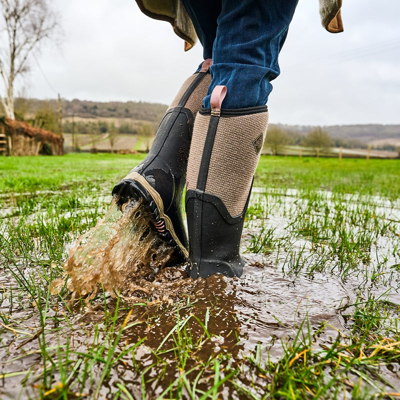 Close up image of a woman standing in a waterlogged field, wearing a pair of Muck Boots wellingtons