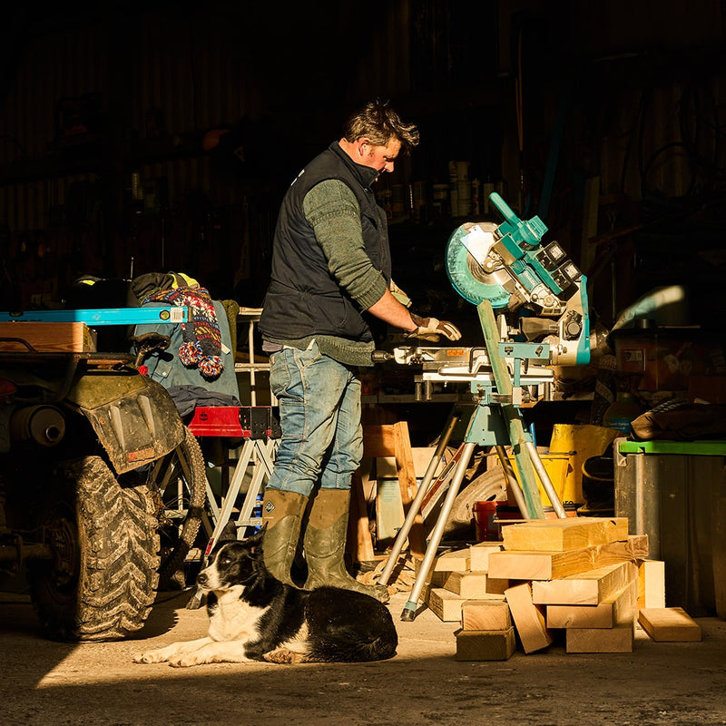 Man wearing a pair of Muck Boots, working in a garage with a border collie dog led down in front of him