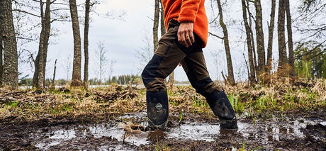 Man walking through a muddy field, wearing a pair of Muck Boots Arctic Sport wellingtons